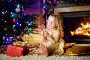 Christmas portrait of happy little girl by a fireplace in a cozy dark living room