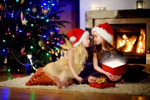 Happy little sisters opening magical Christmas gift by a fireplace